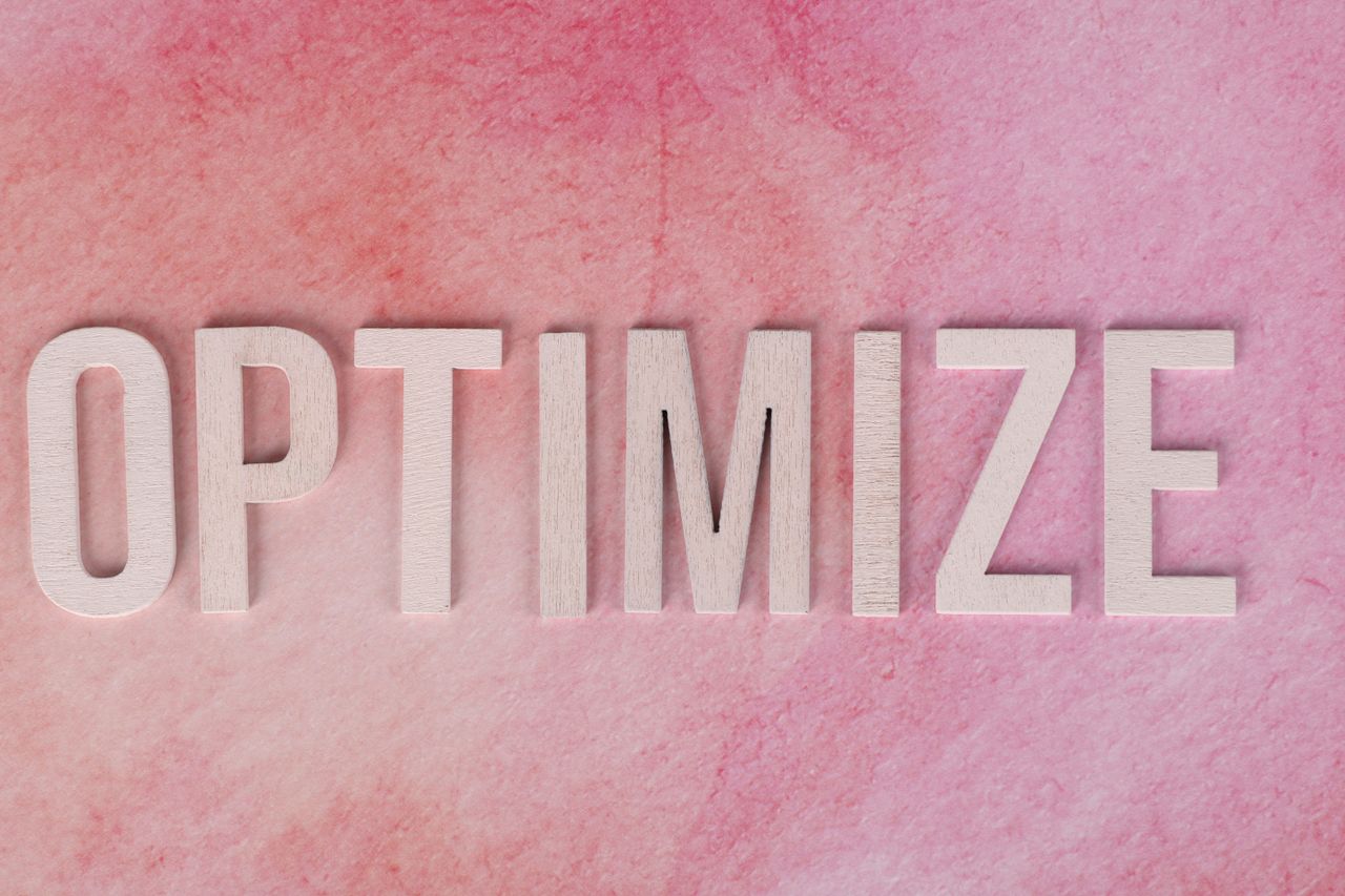 Creative display of the word OPTIMIZE on a pink textured surface.